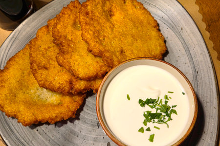 Golden brown crispy potato latkes served on a ceramic plate alongside a bowl of creamy sour cream topped with fresh herbs. ideal for festive gatherings or comforting family meals, these latkes embody traditional and delicious cuisine.の写真素材