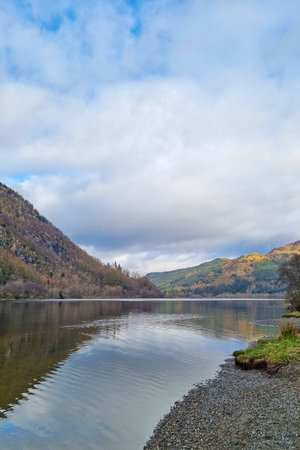 Serenity envelops this lakeside scene as gentle ripples reflect the cloudy sky and autumn foliage. rolling hills frame the calm water, creating a peaceful atmosphere ideal for contemplation and relaxation.の写真素材