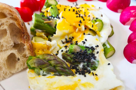 Celebrate a spring-inspired brunch with poached eggs garnished with black sesame seeds and asparagus. complemented by artisan bread and vibrant radishes, this dish offers a fresh and colorful culinary experience.の写真素材