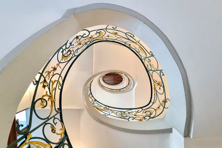 Elegant spiral staircase featuring intricate golden and green ironwork in a historic building. the architectural design blends classical elements with modern elegance, showcasing craftsmanship and aesthetic appeal.の写真素材