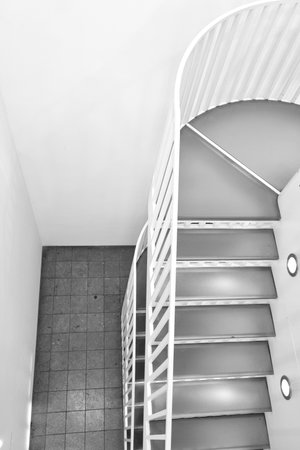 Black and white photograph depicting a modern spiral staircase with a minimalist design. the geometric lines and curves create an elegant composition, offering a sense of movement and sophistication within a clean architectural space.の写真素材