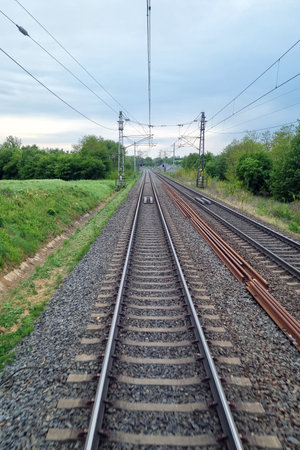 Railway tracks lead into the distance flanked by lush greenery and cloudy skies, emphasizing travel, journey, and exploration. power lines and steel rails create a sense of industrial progress and connectivity.の写真素材