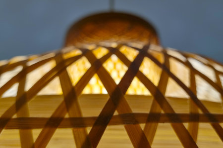 A close-up view of a woven bamboo pendant light showcases its intricate lattice pattern. the warm, soft glow from the light bulb enhances the natural texture and creates a cozy ambiance, suitable for modern interior design.の写真素材