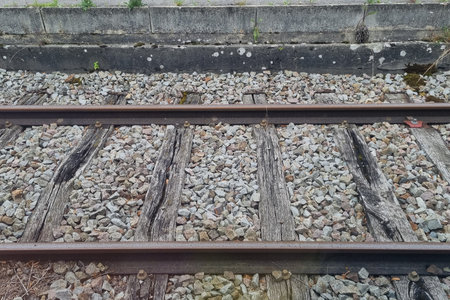 A close-up view of a rustic railroad track featuring weathered wooden sleepers and scattered gravel...