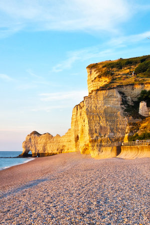 Cliffs bathed in warm golden light during sunset, overlooking a pebble beach and calm sea. the scenic view natural beauty of coastal landscapes, ideal for travel, nature, and seascape themes.の写真素材