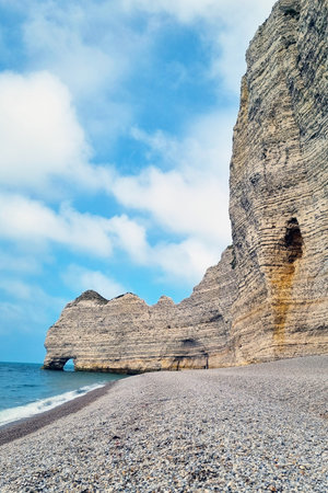 Coastal landscape featuring towering cliffs and a tranquil pebble beach set against a vibrant blue sky. the picturesque scene highlights the natural erosion patterns and the blend of earth and sea. ideal for travel and nature themes.の写真素材