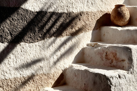Sunlit stone steps create a rustic mediterranean ambiance, enhanced by a textured clay pot. shadows cast by nearby structures add depth and contrast, the rough texture of the wall and steps. Generative AIの素材