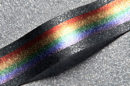 A vivid rainbow-colored tape lies diagonally across a glittery silver background, creating a striking contrast. the shimmering texture and vibrant colors evoke themes of creativity, celebration, and festive decoration, perfect for design or festive purposes. Generative AIの素材