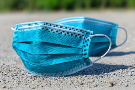 Two blue disposable face masks lie abandoned on a gravel surface, emphasizing the environmental impact of personal protective equipment waste. the image conveys themes of pollution, health, and pandemic-related challenges. Generative AIの素材