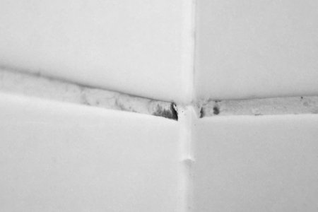 Detailed view of dirty grout between white tiles, the need for cleaning or renovation. the image focuses on the intersection of the tiles, emphasizing the contrast between the bright tiles and the darkened grout lines.の写真素材