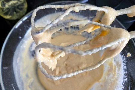 Close-up view of cake batter on a mixer in a glass bowl, capturing the dynamic preparation process....