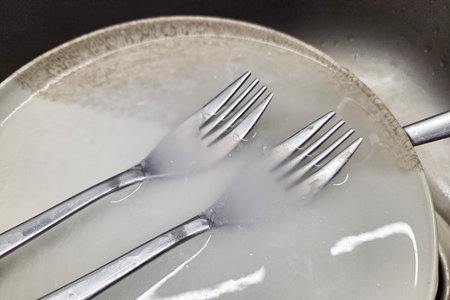 Kitchen Cleaning Scene with Utensils and Soapy Water in Metal Sinkの写真素材