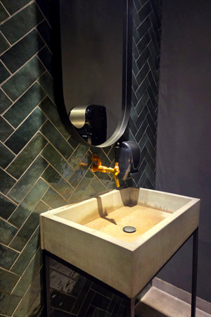 A modern restroom features a concrete sink with a circular drain. Above the sink, there is a wall-mounted mirror. The green tiles on the wall add texture to the space.の写真素材