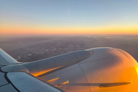 Dawn's gentle hues illuminate the airplane's wing as it soars above vast terrains. the rising sun...