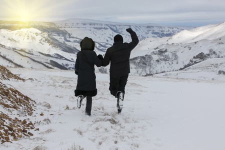 Happy couple in snowy mountains is running towards the sunの写真素材