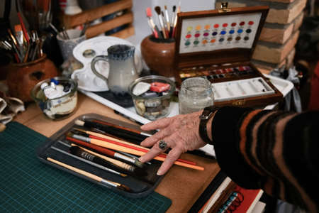 Old womans hand takes paintbrushes for watercolor paintingの写真素材