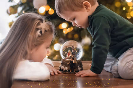 Sister and brother looking at a glass ball with a scene of the nativity of Jesus Christ in a glass ball on a Christmas treeの写真素材