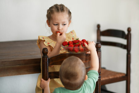 Two young girls eating strawberries in living room smilingの写真素材