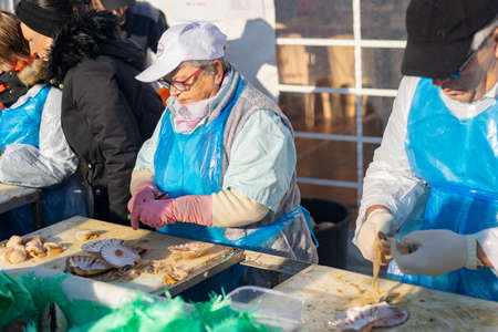 DIEPPE, FRANCE - NOVEMBER 17, 2019: Men and women open and clean scallops for sale at a Fair of Herring and scallop shell in a port of Dieppeのeditorial素材