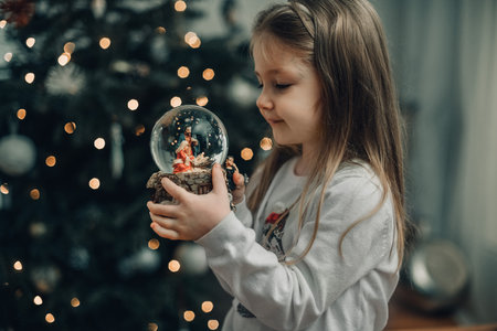 Girl looking at a glass ball with a scene of the birth of Jesus Christ in a glass ball on a Christmas treeの写真素材