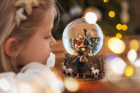 Girl looking at a glass ball with a scene of the nativity of Jesus Christ in a glass ball on a Christmas treeの写真素材