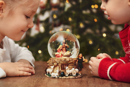 Children looking at a glass ball with a scene of the birth of Jesus Christ near christmas treeの写真素材