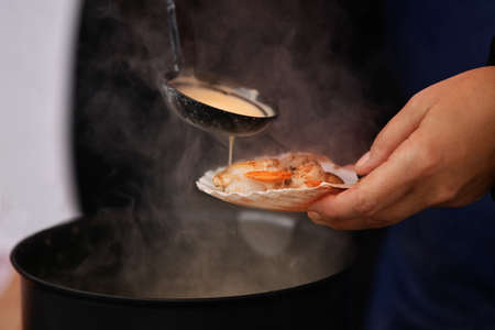 The seller pours white sauce on the scallopsの写真素材