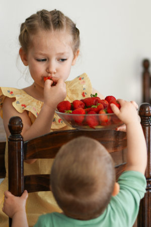Two young girls eating strawberries in living room smilingの写真素材