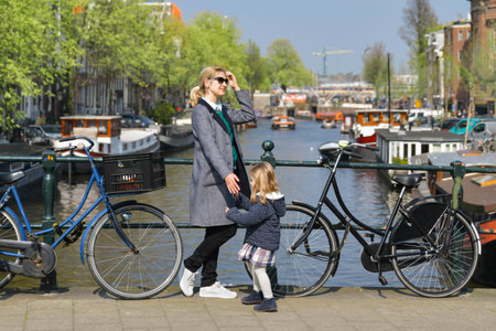 Blonde Dutchwoman mother with her daughter near the bicycle on the bridge over the water channel in Amsterdam cityの写真素材