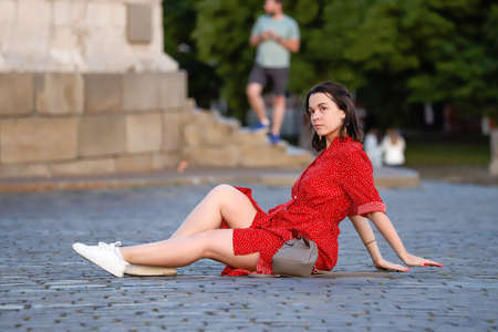 Girl in a red dress posing sitting on the cobblestones, Red Square, summer day. Russia Moscow June 2020.のeditorial素材
