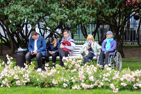 People sit on a bench on a summer day in a garden in St. Petersburg. Russia, Saint Petersburg July...