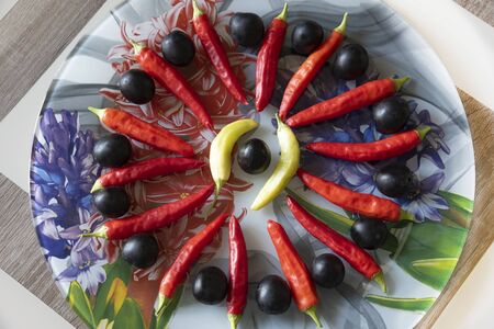 On a plate of stained glass, chili peppers are arranged in a circle, and between the peppers lies a blackthorn fruit.の写真素材