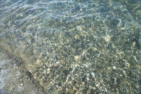 Sea pebbles are clearly visible through the clear water at the bottom along the coast.の写真素材