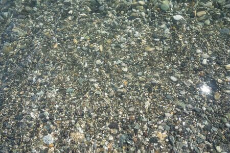 Sea pebbles are clearly visible through the clear water at the bottom along the coast.の写真素材