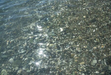 Sea pebbles are clearly visible through the clear water at the bottom along the coast.の写真素材