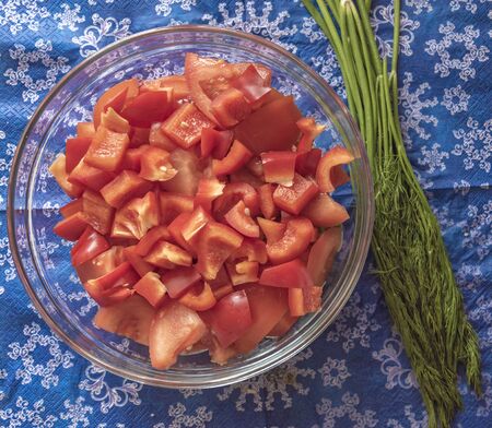A salad of fresh tomatoes and red bell peppers with fresh herbs is on the table in a glass bowl.の写真素材