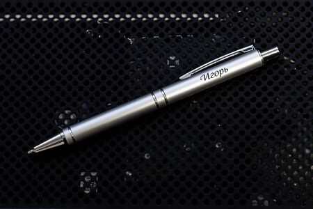 A metal name pen lies on a dark techno background, illuminated by upper-side light.の写真素材