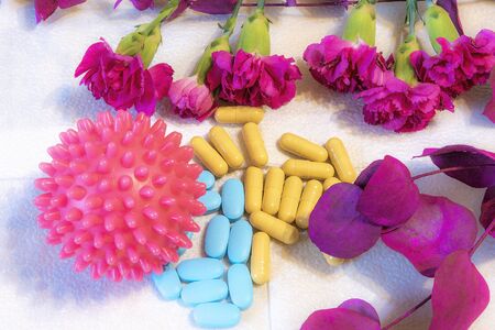 Coronavirus should not be underestimated, therefore it is depicted large in the foreground and attracts red color, in front of it are pills that symbolize the treatment, and flowers and a twig with leaves are life.の写真素材