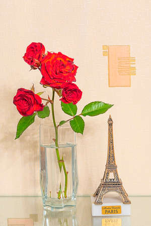 Close-up still life of a rose in a glass glass on a glass shelf with a statuette of the Eiffile Tower.の写真素材