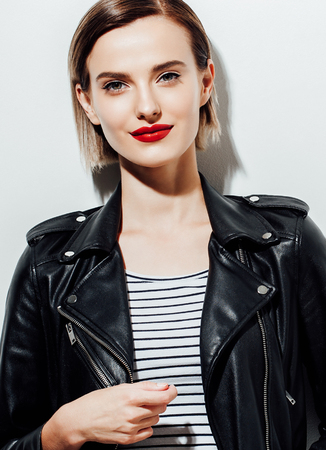 Glamorous young woman in black leather jacket on white background with mobile phoneの写真素材