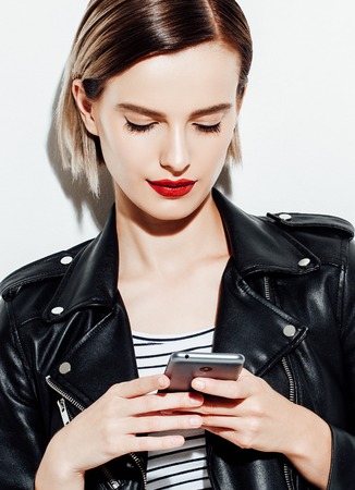 Glamorous young woman in black leather jacket on white background with mobile phone