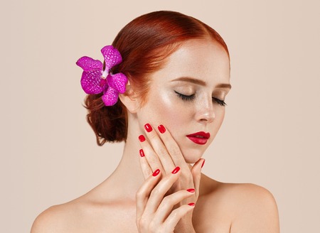 Beautiful woman portrait with flower in hair perfect make up manicure red lips and nails on beige background isolatedの写真素材