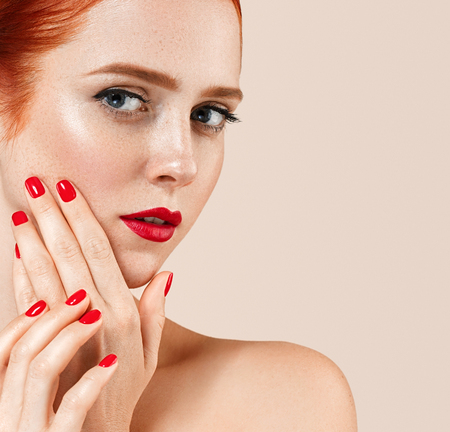 Beautiful red hair woman portrait with perfect make up manicure red lips and nails. Studio shot.の写真素材