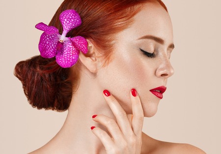 Beautiful woman portrait with flower in hair perfect make up manicure red lips and nails on beige background isolatedの写真素材