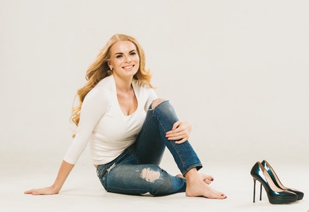 Amazing woman blonde curly hair portrait jeans fashion beautiful sitting on floorの写真素材