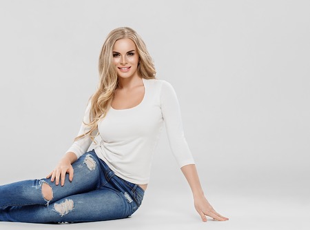 Beautiful woman blonde curly hair sexy portrait jeans fashion full length sitting on floor. Stuio shot.の写真素材