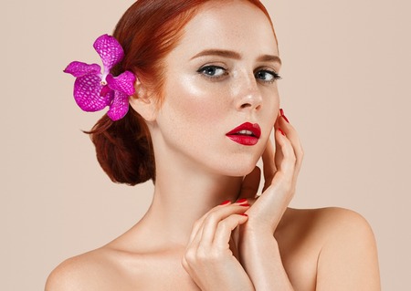 Beautiful woman portrait with flower in hair perfect make up manicure red lips and nails on beige background isolatedの写真素材