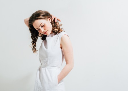 Fashion woman with freckles face, curly hair in white dress on white backgroundの写真素材