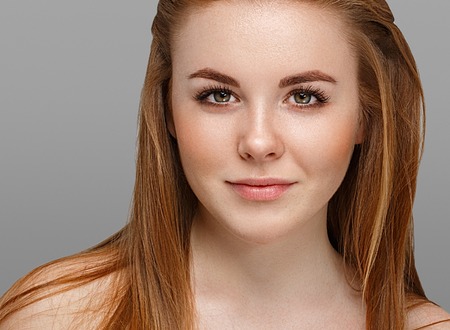 Beautiful woman face close up portrait young with red hair on gray background. Studio shot.の写真素材