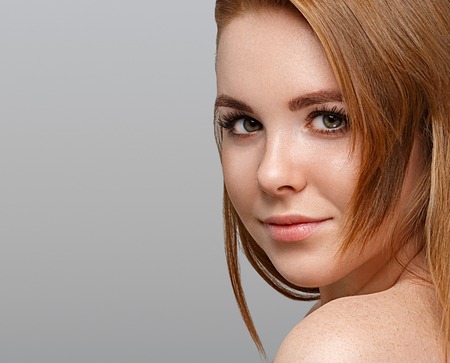 Beautiful woman face close up portrait young with red hair on gray background. Studio shot.の写真素材